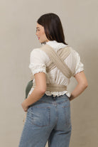 Woman wearing a beige woven wrap carrier on a plain background