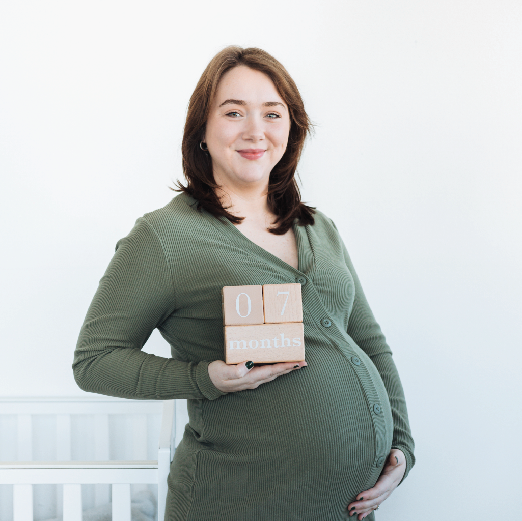 Pregnant woman holding wooden blocks with '07 months' on a white background