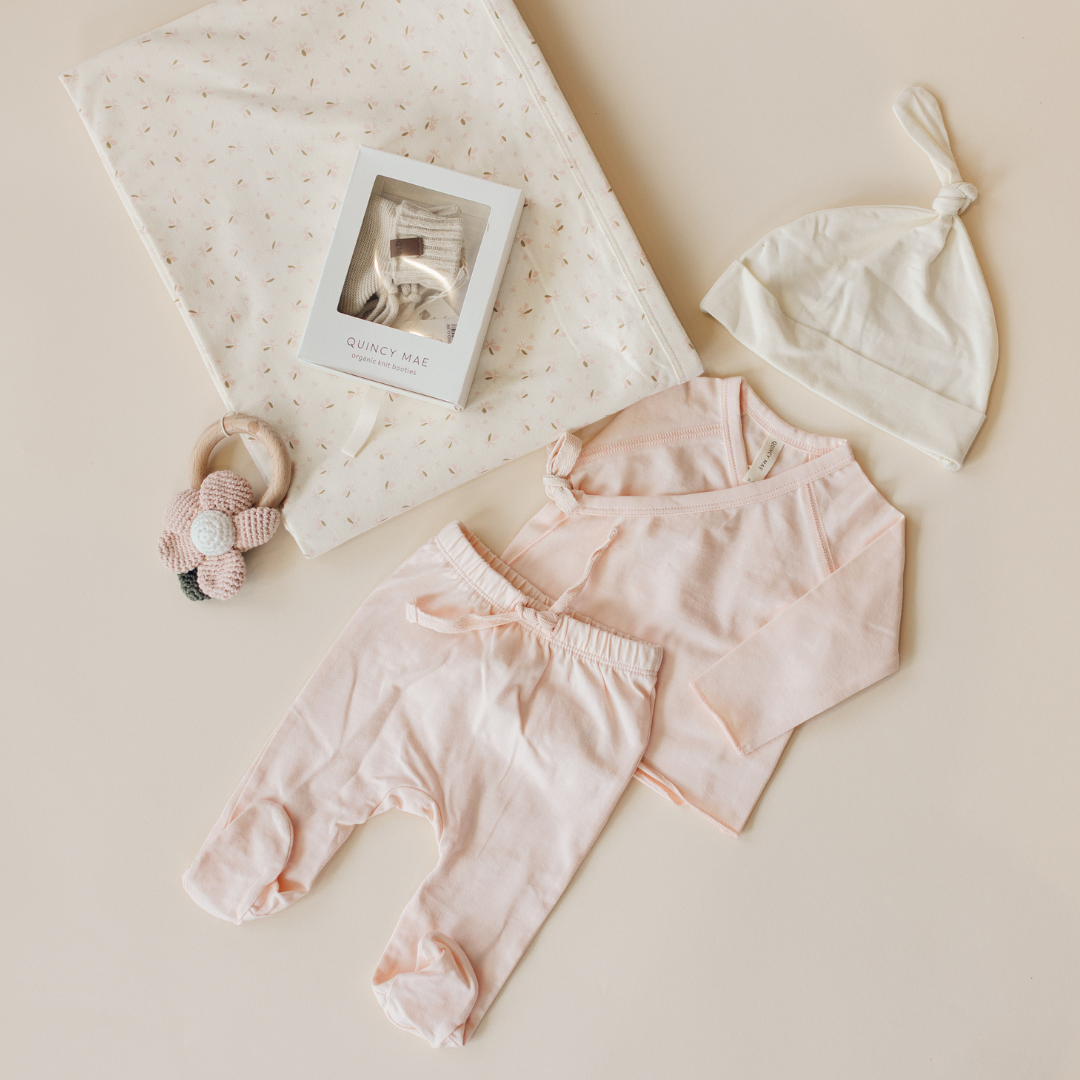Baby clothing set with pink pants, white hat, and headband on a beige background