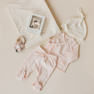 Baby clothing set with pink pants, white hat, and headband on a beige background