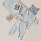 Baby clothing set with outfit, hat, and toys on a beige background