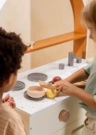 Two children playing with a wooden toy kitchen set.