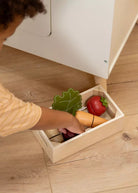 Child playing with toy vegetables in a wooden box on a wooden floor