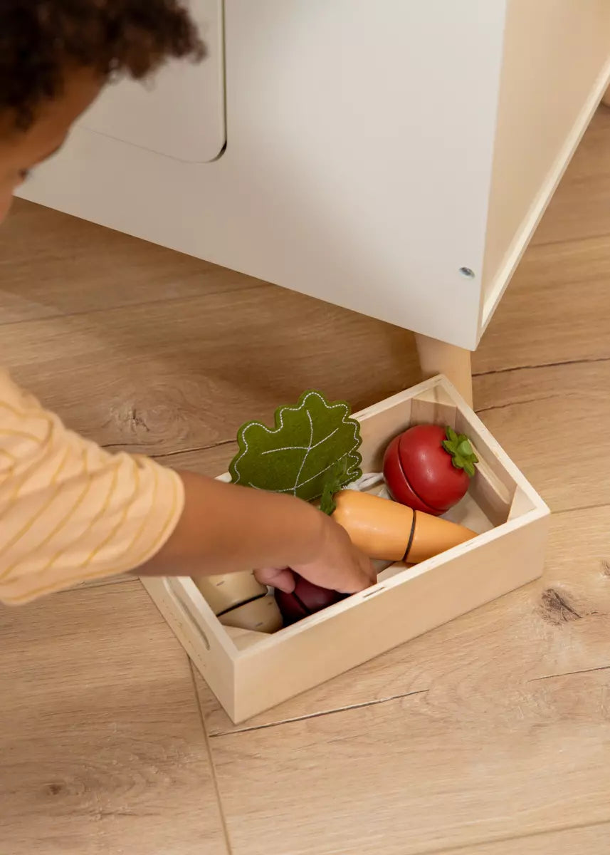 Child playing with toy vegetables in a wooden box on a wooden floor
