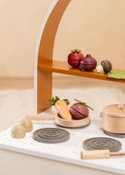 Wooden toy kitchen set with pots, pans, and vegetables on a shelf against a beige background
